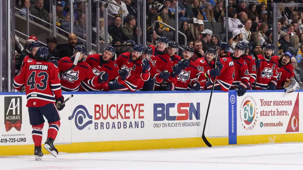 Toledo Walleye hockey players in red uniforms celebrating on the bench during a game in front of cheering fans at an ice arena