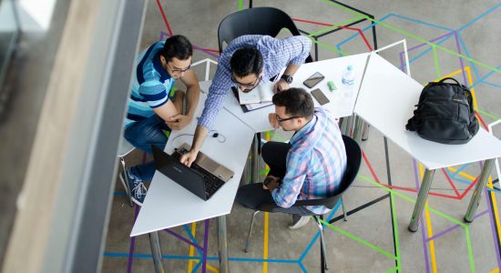 Three men collaborating over a laptop in a modern, geometric-themed office space.