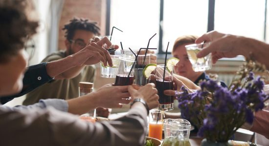 A group of friends toasting drinks in a warm, cozy indoor setting with food and flowers.